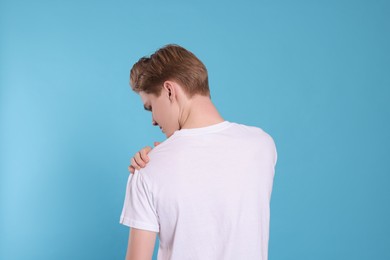 Teenage boy suffering from pain in shoulder on light blue background, back view. Arthritis symptom