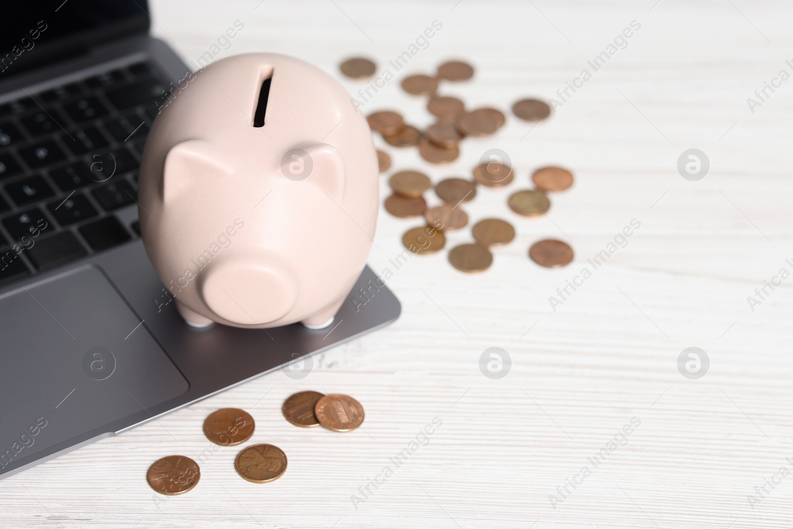 Photo of Piggy bank, coins and laptop on white table. Space for text