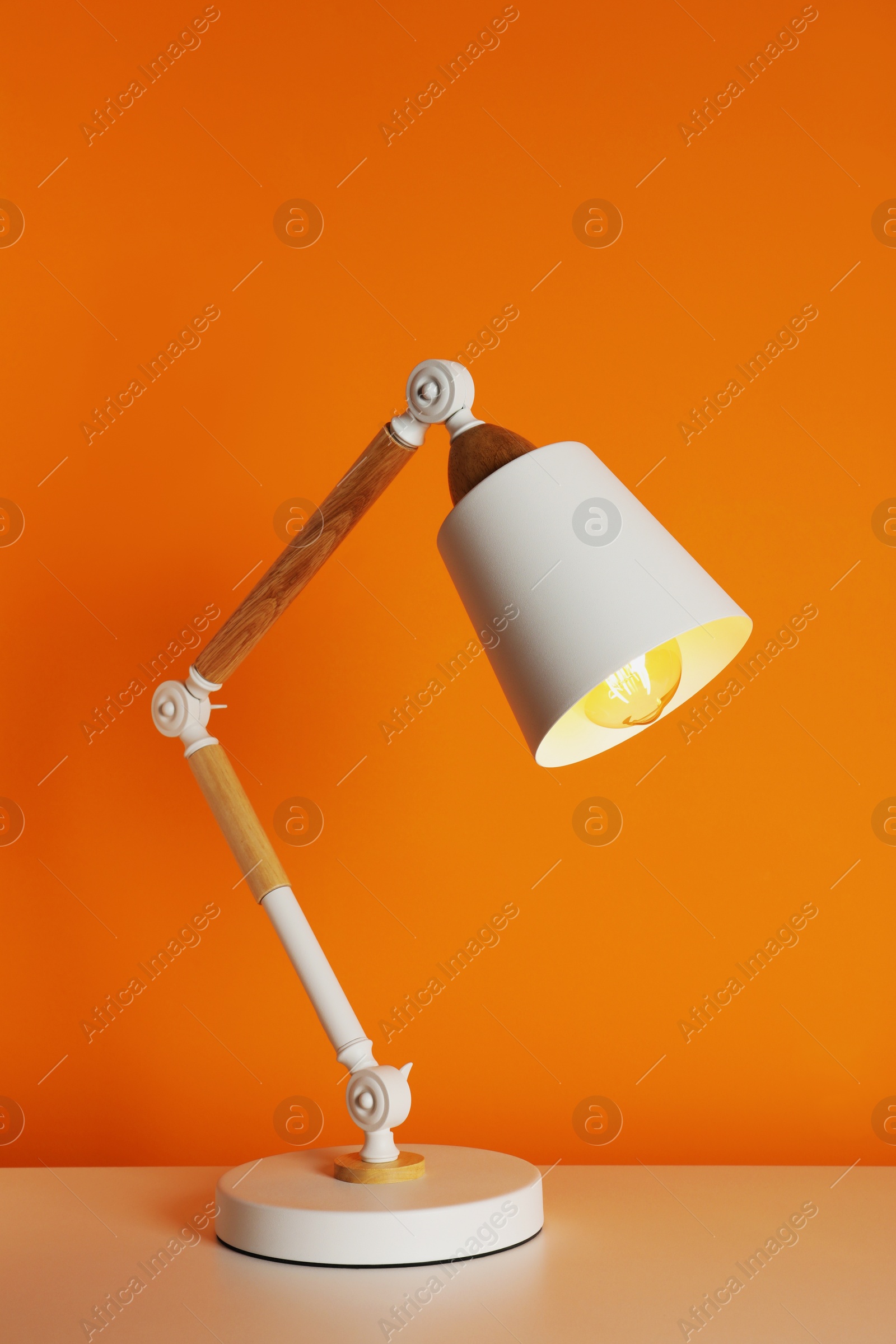 Photo of Stylish modern desk lamp on white table near orange wall