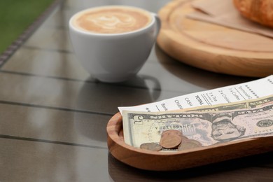 Tips, receipt and cup with coffee on wooden table, closeup