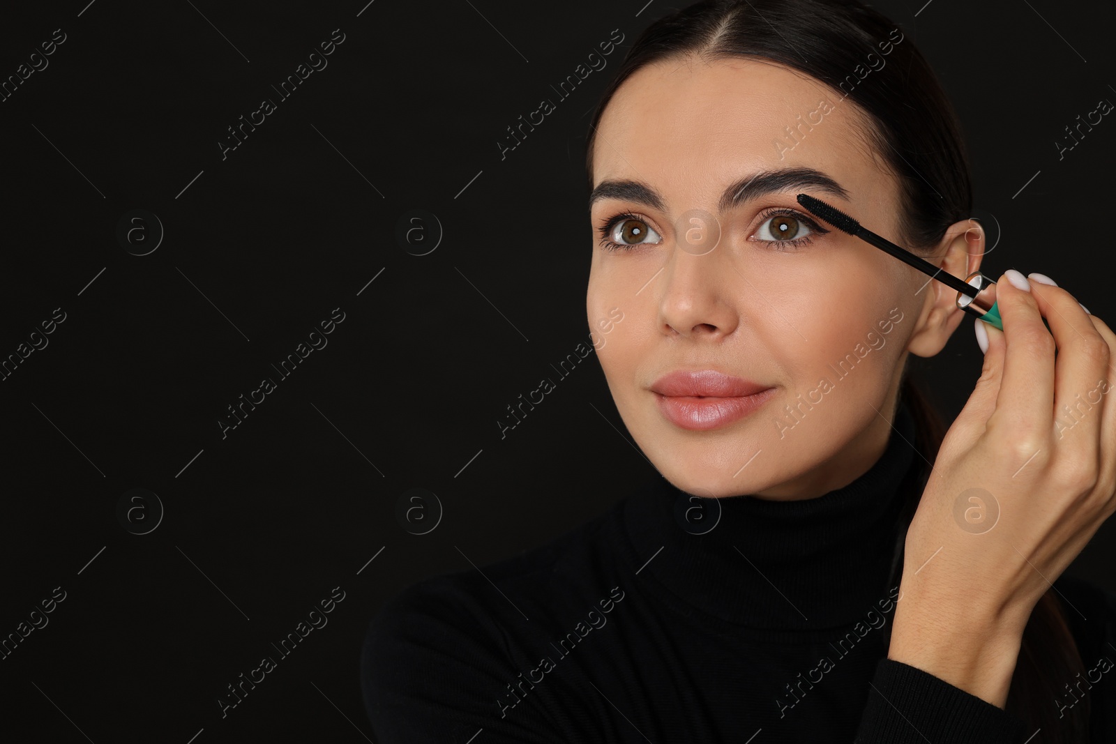 Photo of Beautiful young woman applying mascara on black background, closeup. Space for text