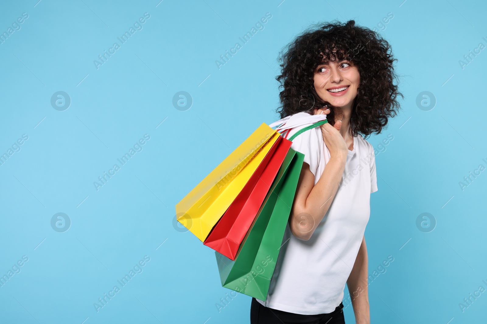 Photo of Happy young woman with shopping bags on light blue background. Space for text