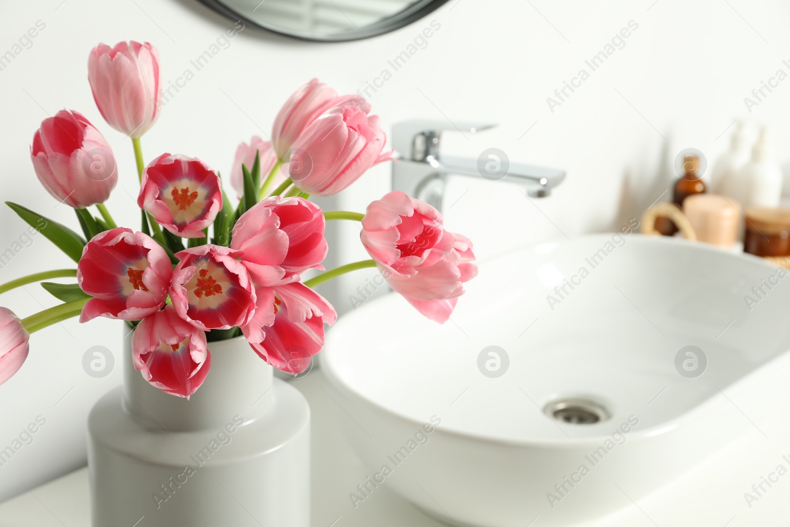 Photo of Vase with beautiful pink tulips and toiletries near sink in bathroom, closeup