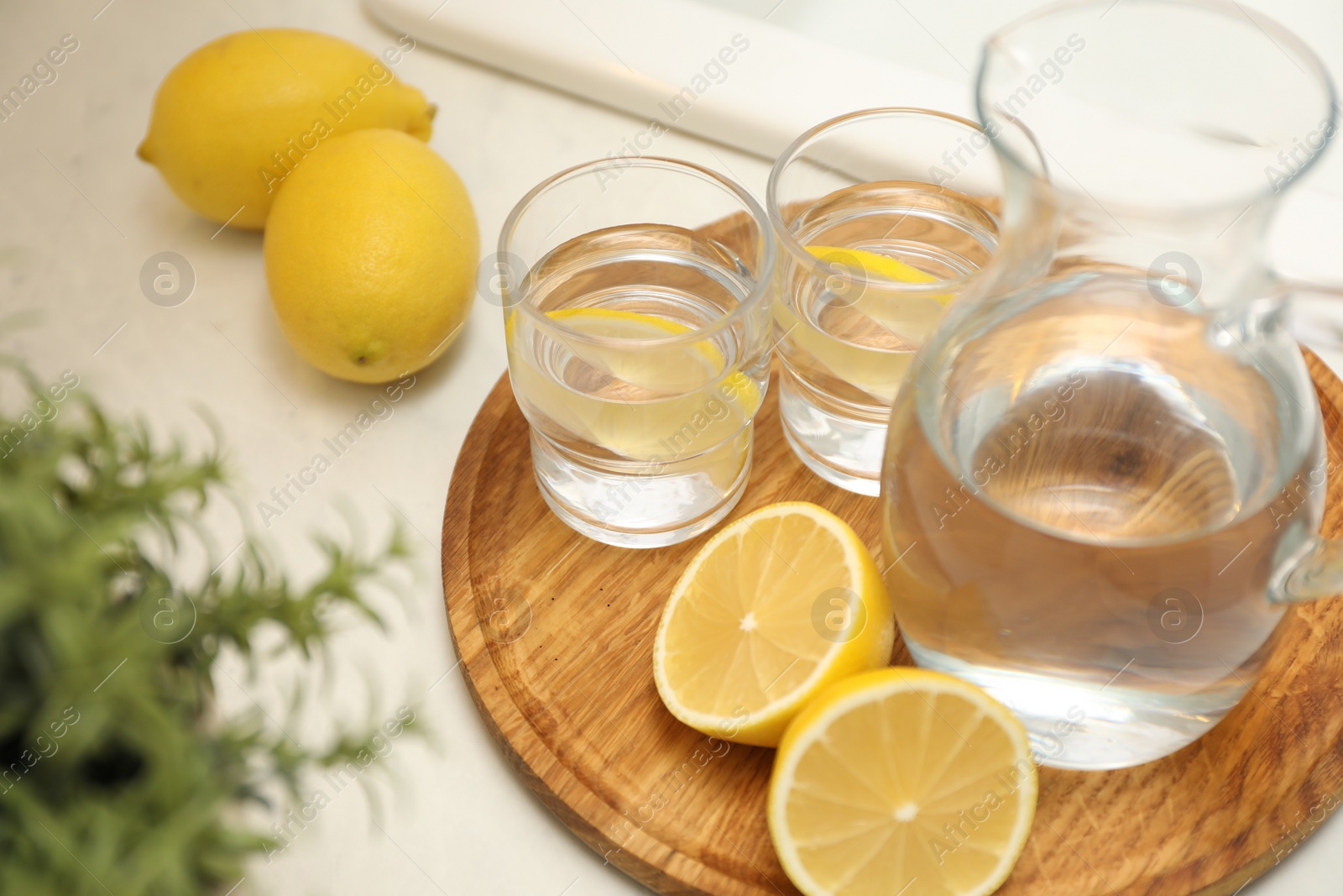 Photo of Jug, glasses with clear water and lemons on white table in kitchen, closeup