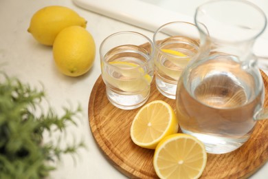 Photo of Jug, glasses with clear water and lemons on white table in kitchen, closeup