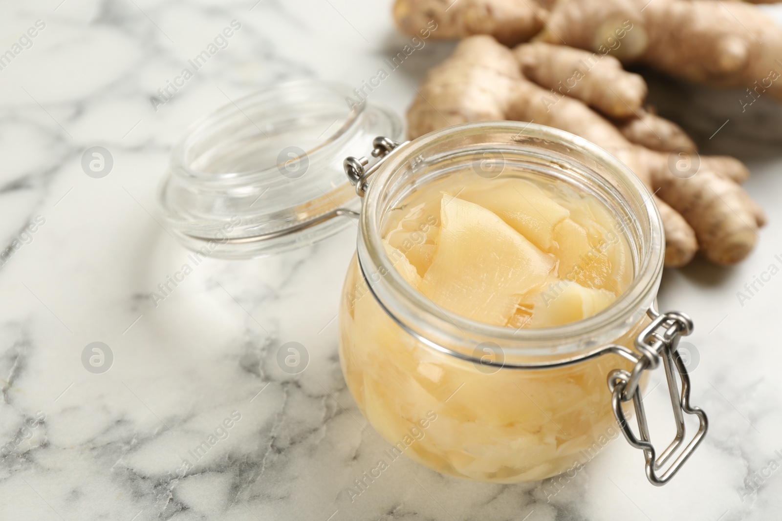 Photo of Spicy pickled ginger and root on white marble table, space for text