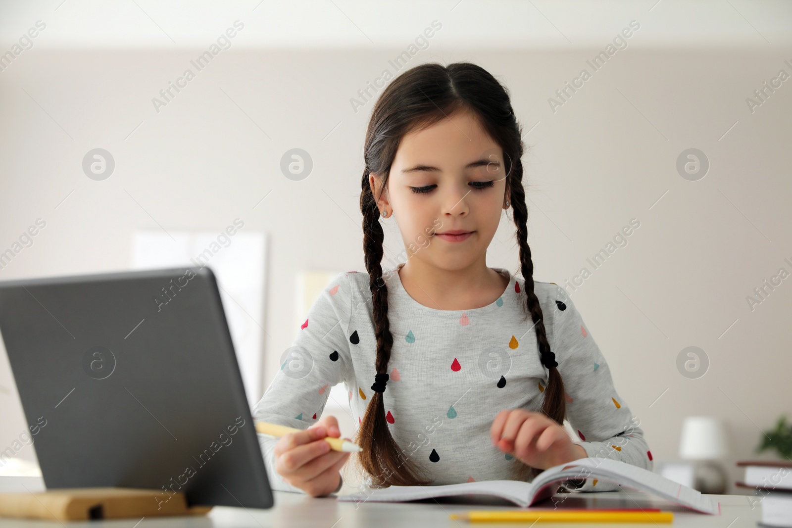 Photo of Little girl doing homework with modern tablet at home