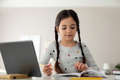 Little girl doing homework with modern tablet at home