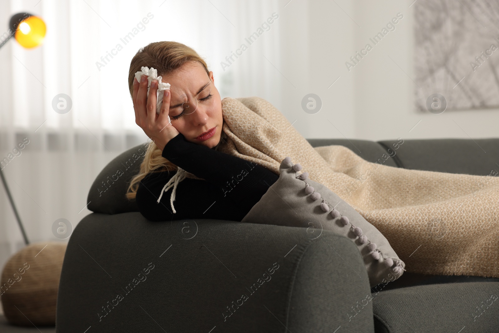 Photo of Sick woman with tissue under blanket on sofa at home. Cold symptoms