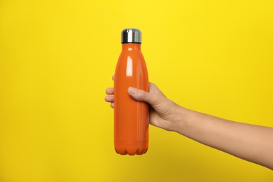Photo of Woman holding modern orange thermos on yellow background, closeup