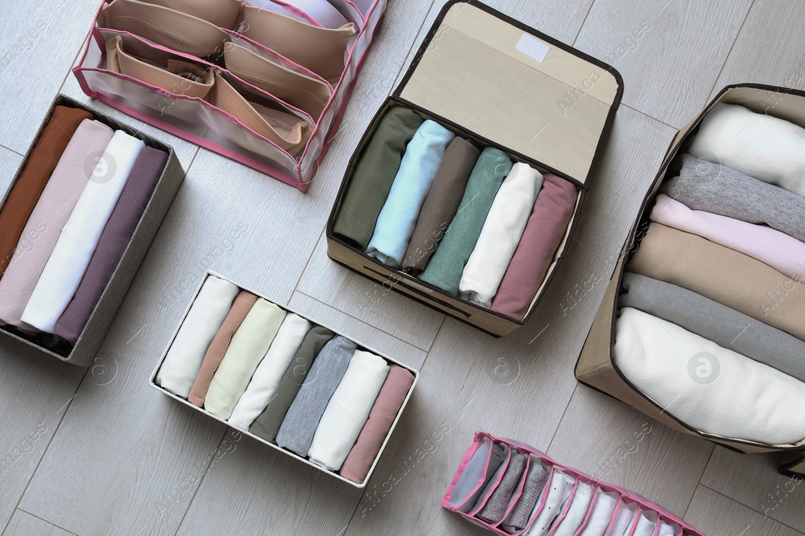 Photo of Different organizers with folded clothes and underwear on white wooden background, flat lay. Vertical storage