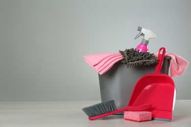 Photo of Bucket with cleaning products and supplies on light table. Space for text