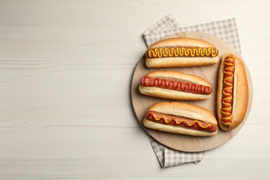 Photo of Fresh delicious hot dogs with sauces on white wooden table, top view. Space for text