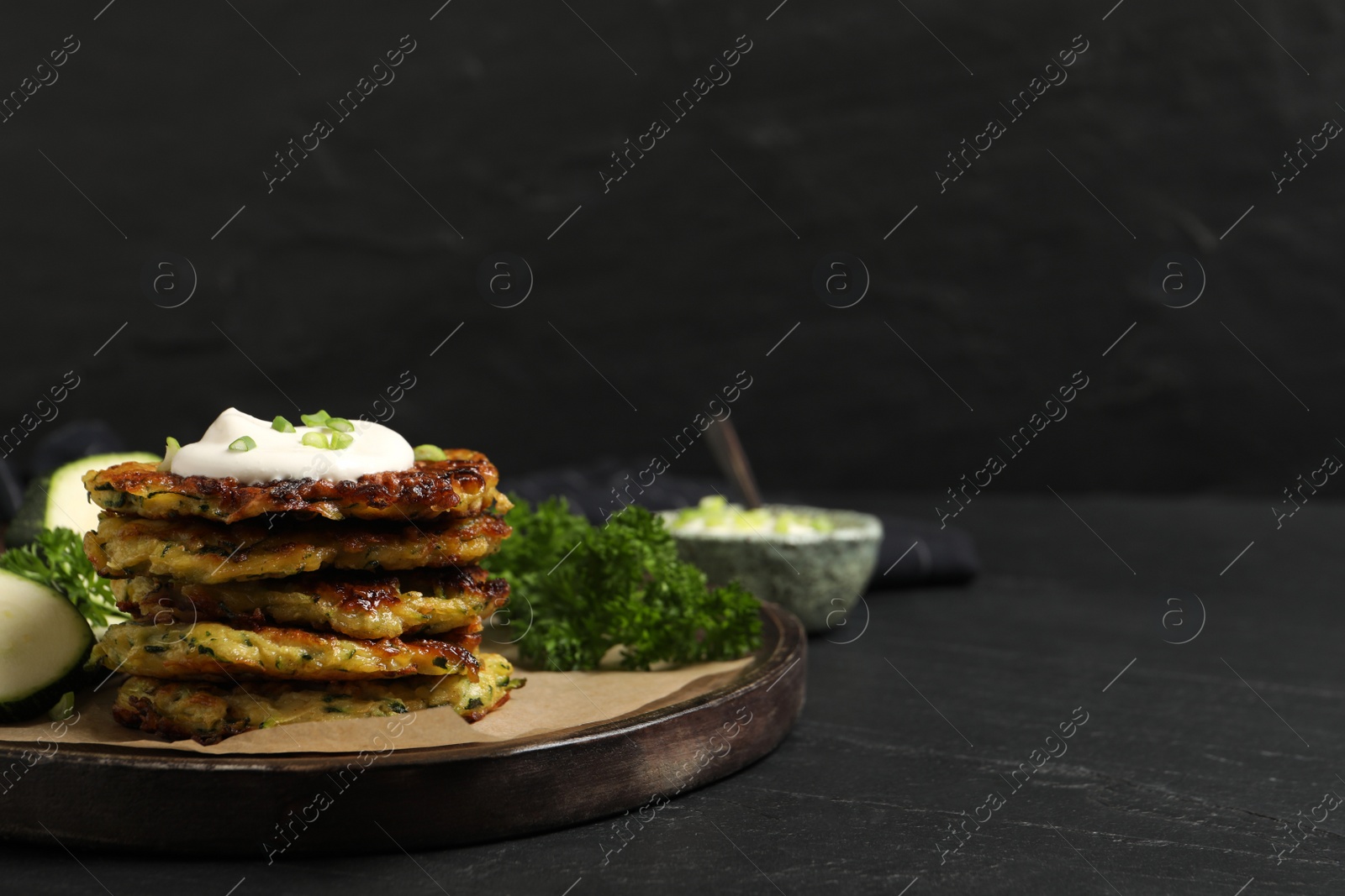 Photo of Delicious zucchini fritters with sour cream served on black table, space for text