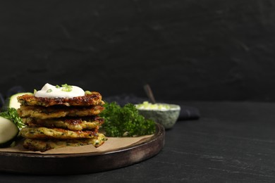 Photo of Delicious zucchini fritters with sour cream served on black table, space for text