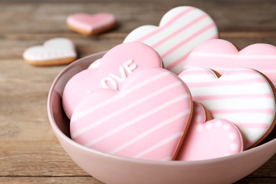 Photo of Decorated heart shaped cookies in bowl on wooden table, closeup. Valentine's day treat