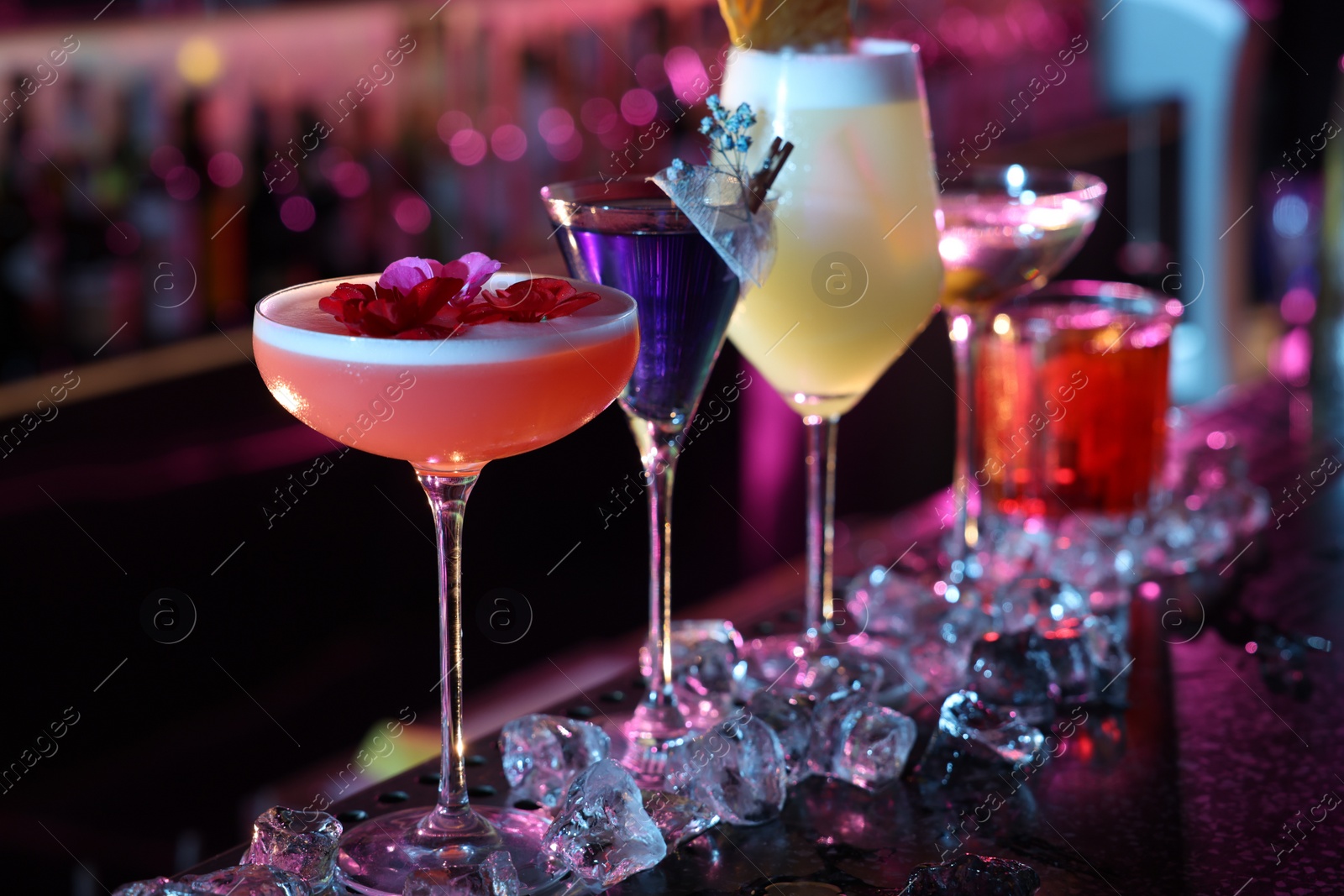 Photo of Different fresh alcoholic cocktails and ice cubes on counter in bar