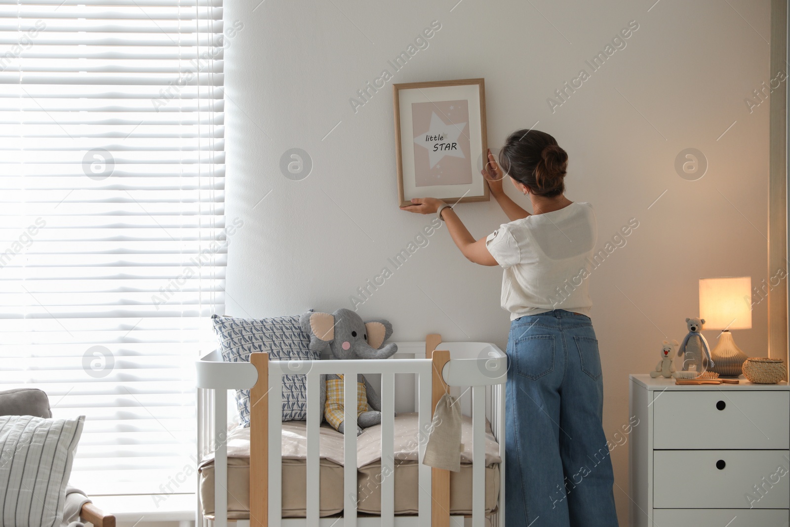 Photo of Decorator hanging picture on wall in baby room. Interior design