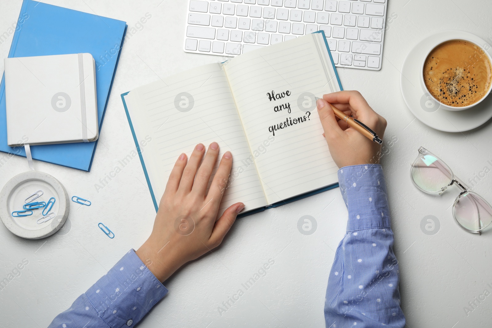 Photo of Woman writing phrase HAVE ANY QUESTIONS in notebook at white table, top view