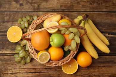 Photo of Wicker basket with different fruits on wooden table, flat lay