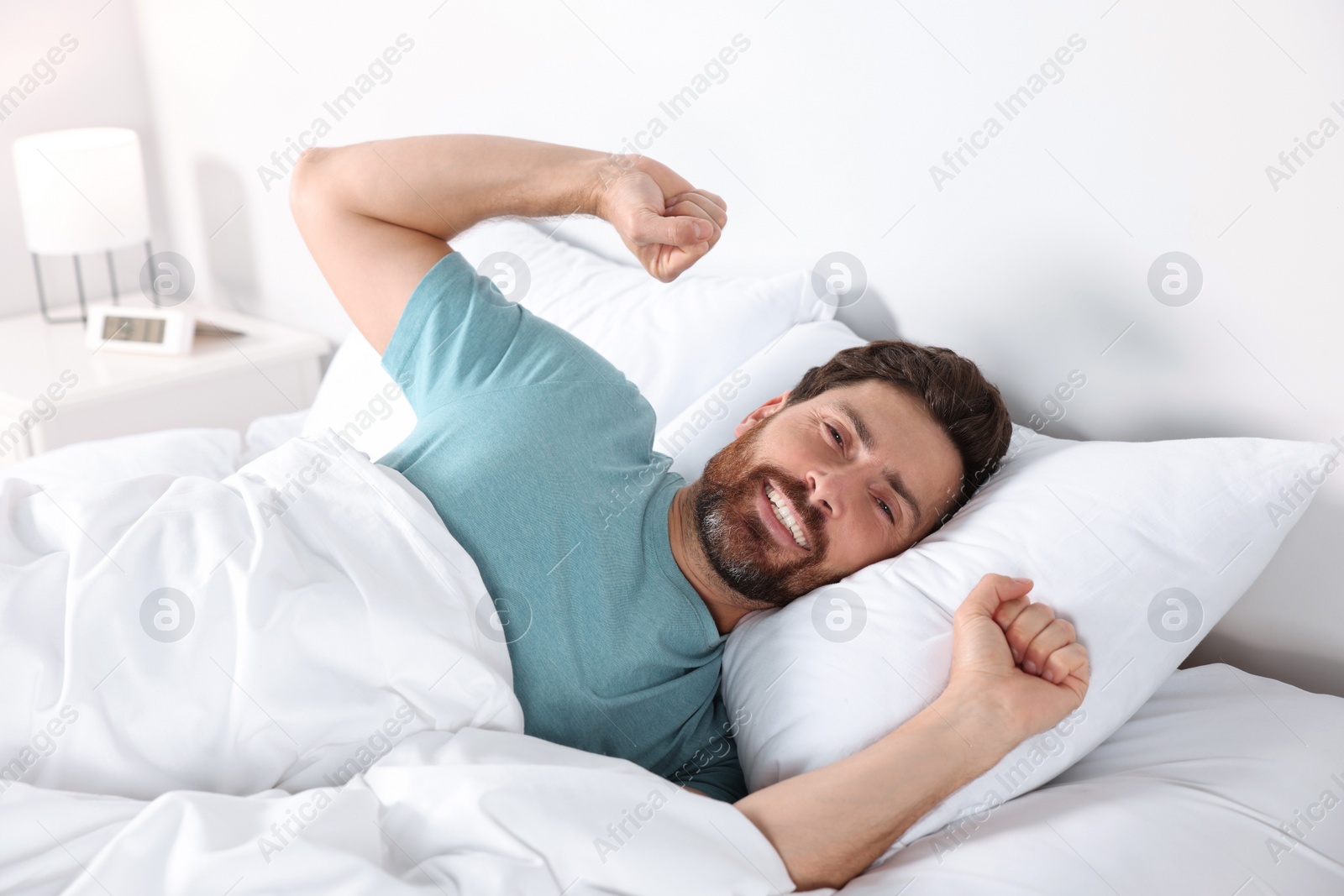 Photo of Happy man stretching on comfortable pillow in bed at home