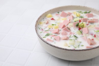 Photo of Delicious cold summer soup (okroshka) with boiled sausage in bowl on white tiled table. Space for text