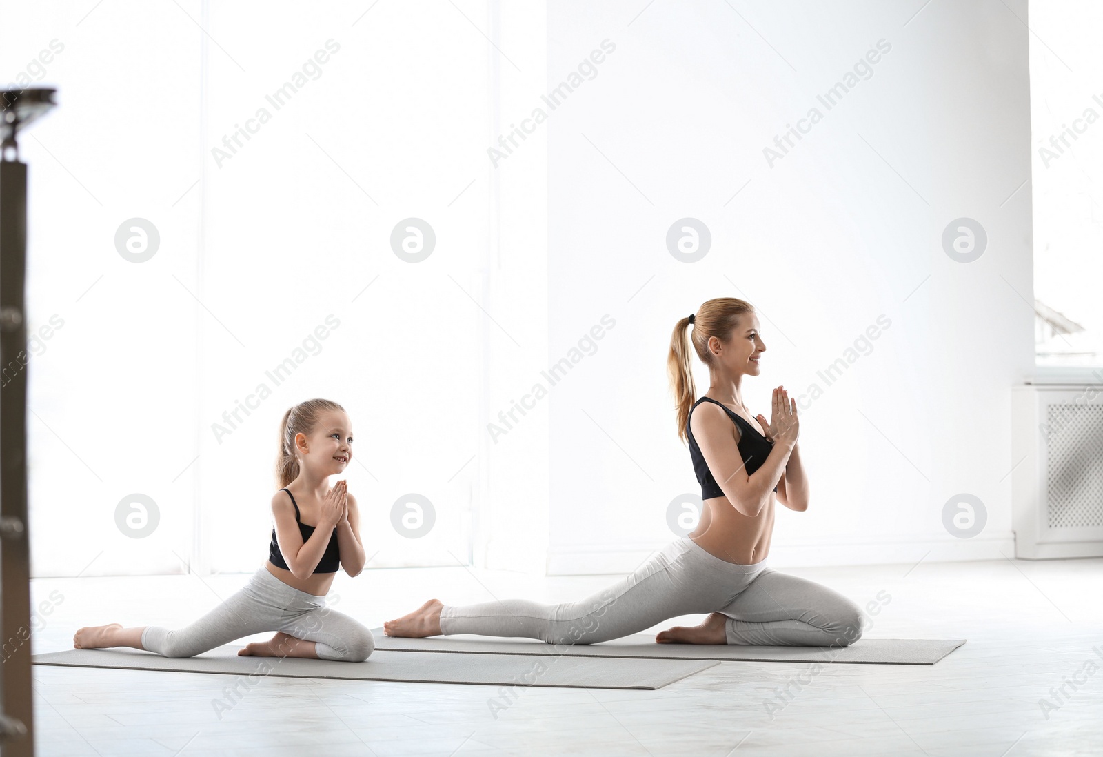 Photo of Mother and daughter in matching sportswear doing yoga together at home