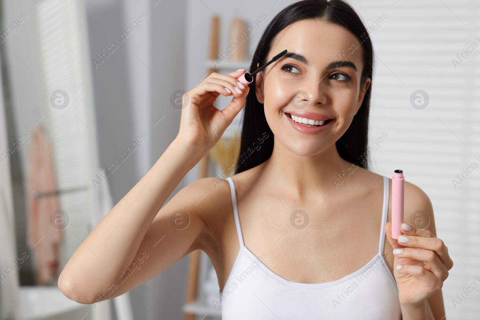 Photo of Beautiful young woman applying mascara with brush indoors