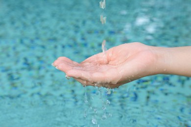 Photo of Water pouring into the girl's hand above pool, closeup