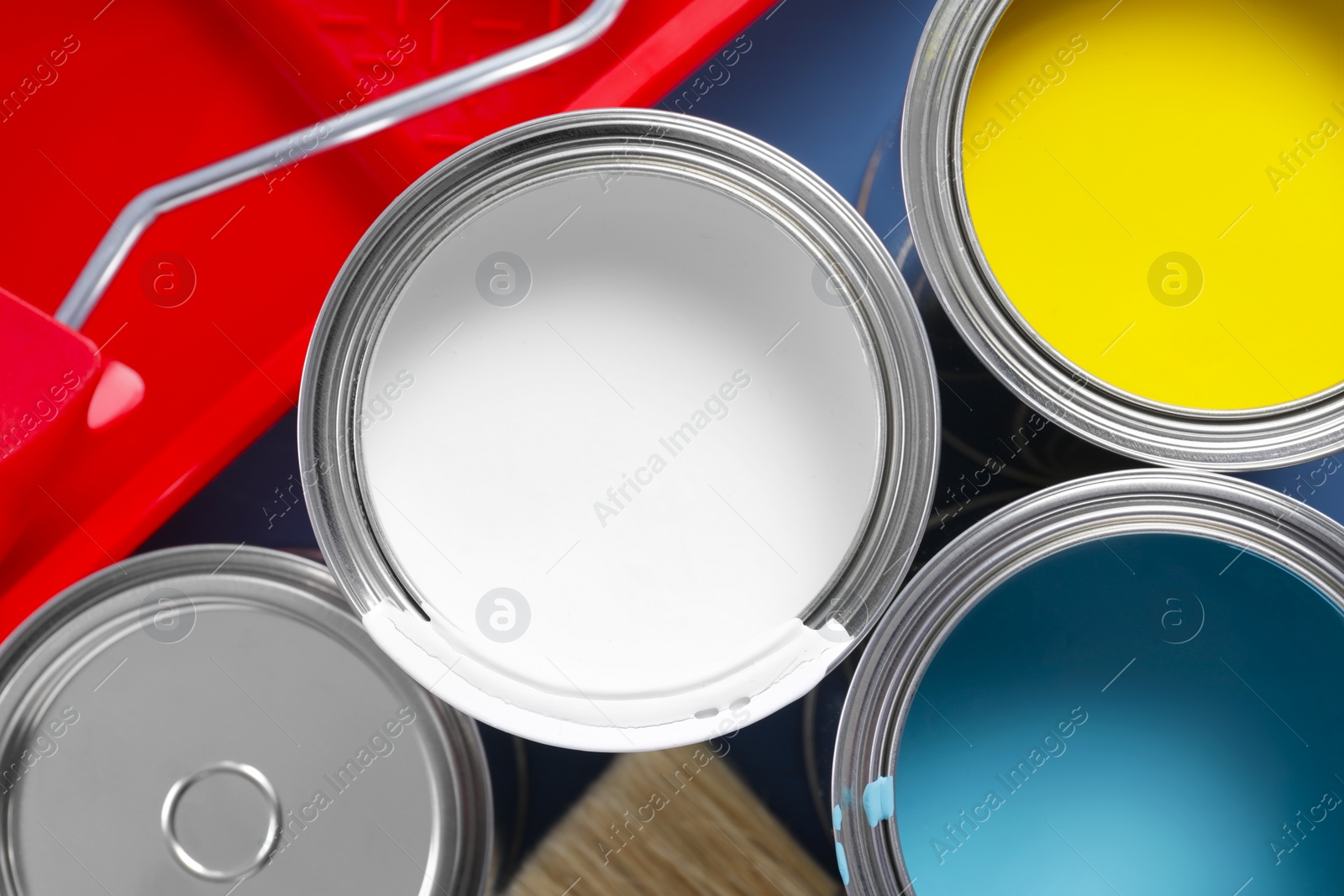 Photo of Cans of paints, brush, roller and tray on blue table, flat lay