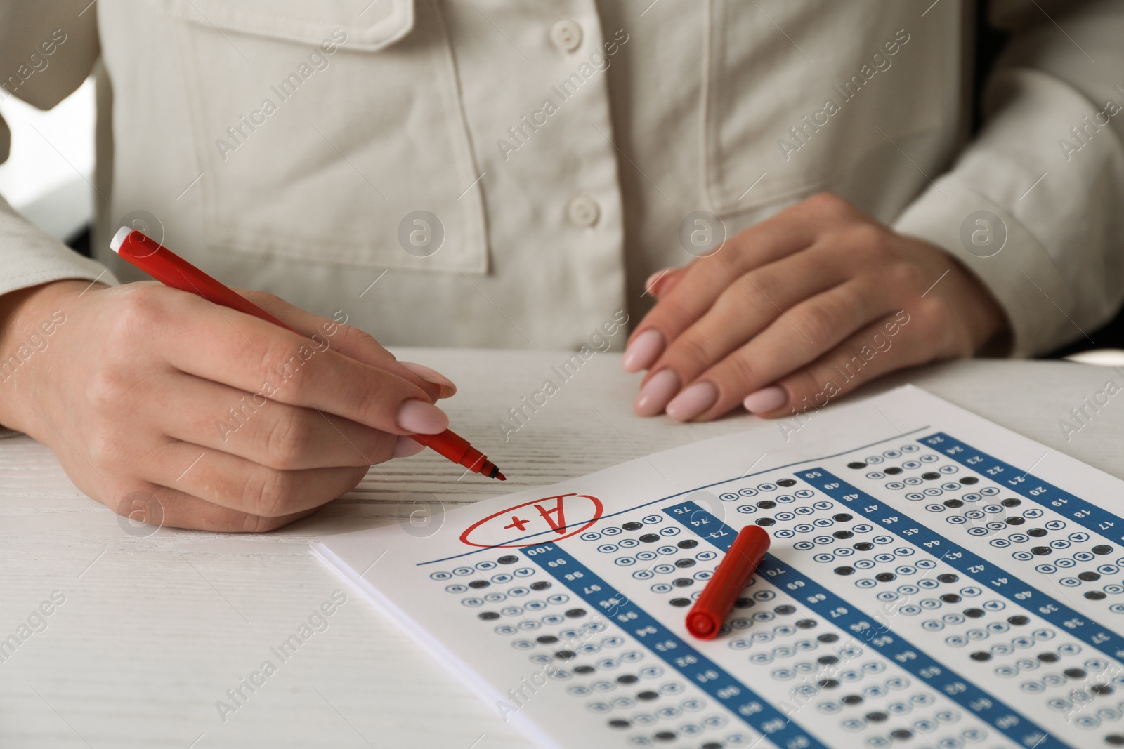 Photo of School grade. Teacher writing letter A with plus symbol on answer sheet at white table, closeup