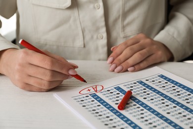 School grade. Teacher writing letter A with plus symbol on answer sheet at white table, closeup