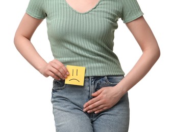 Woman holding sticky note with drawn sad face and suffering from cystitis on white background, closeup