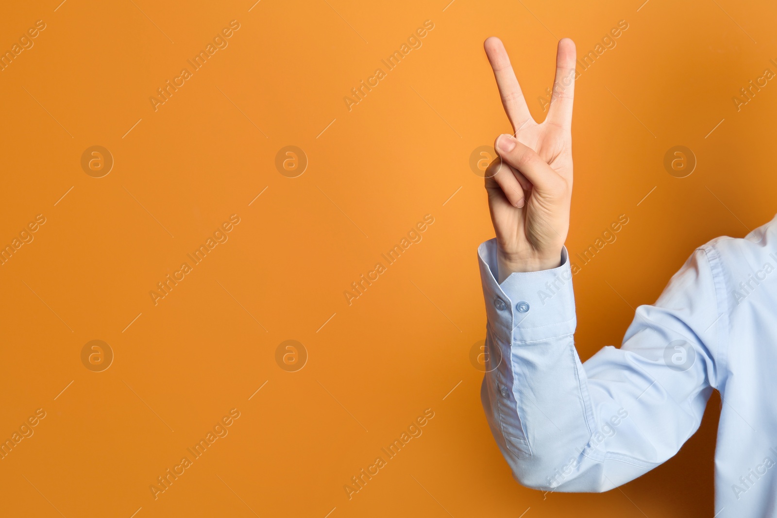 Photo of Young woman showing victory gesture on color background. Space for text