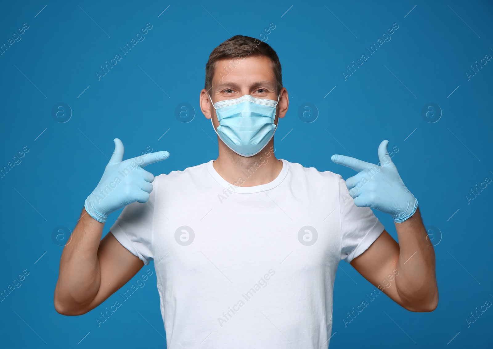 Photo of Male volunteer in mask and gloves on blue background. Protective measures during coronavirus quarantine