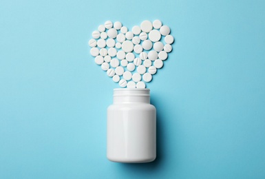 Heart made of pills and container on color background, top view