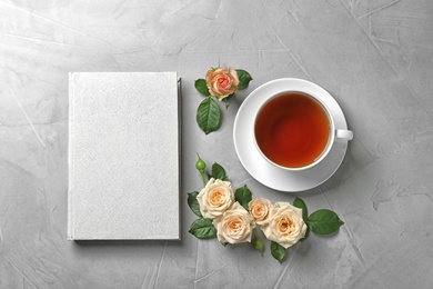 Flat lay composition with hardcover book and flowers on grey table