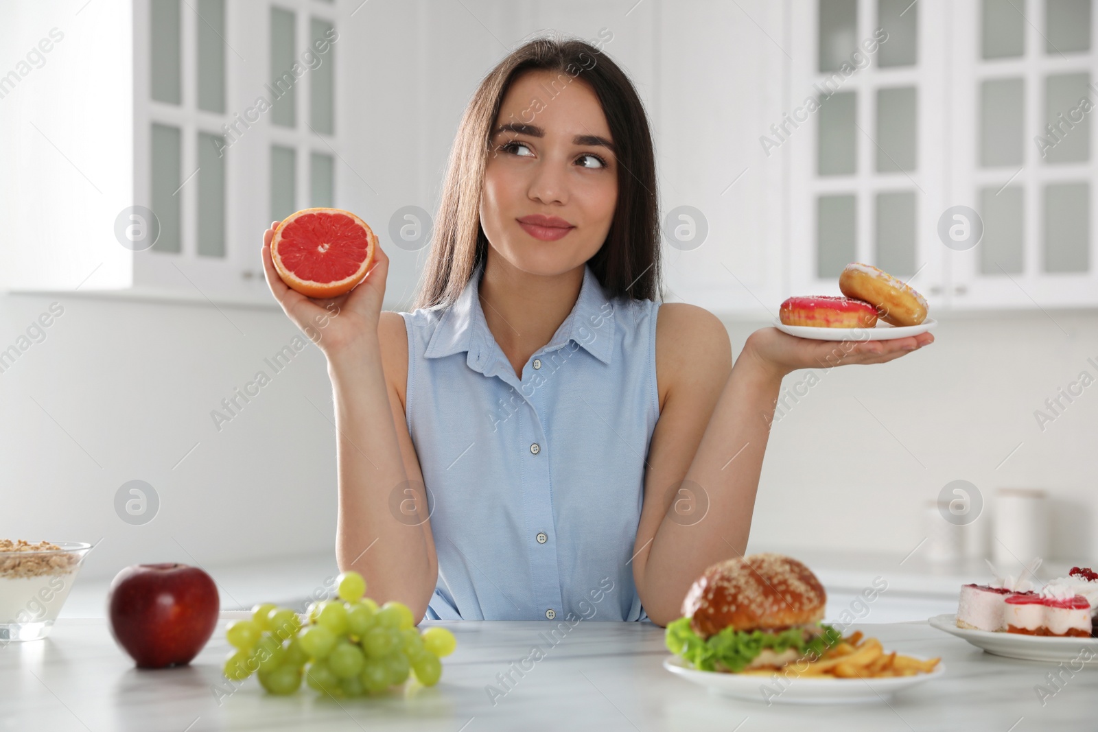 Photo of Woman choosing between grapefruit and doughnuts in kitchen