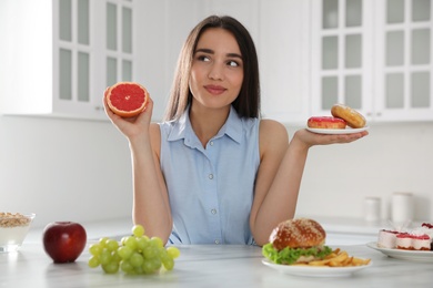 Photo of Woman choosing between grapefruit and doughnuts in kitchen