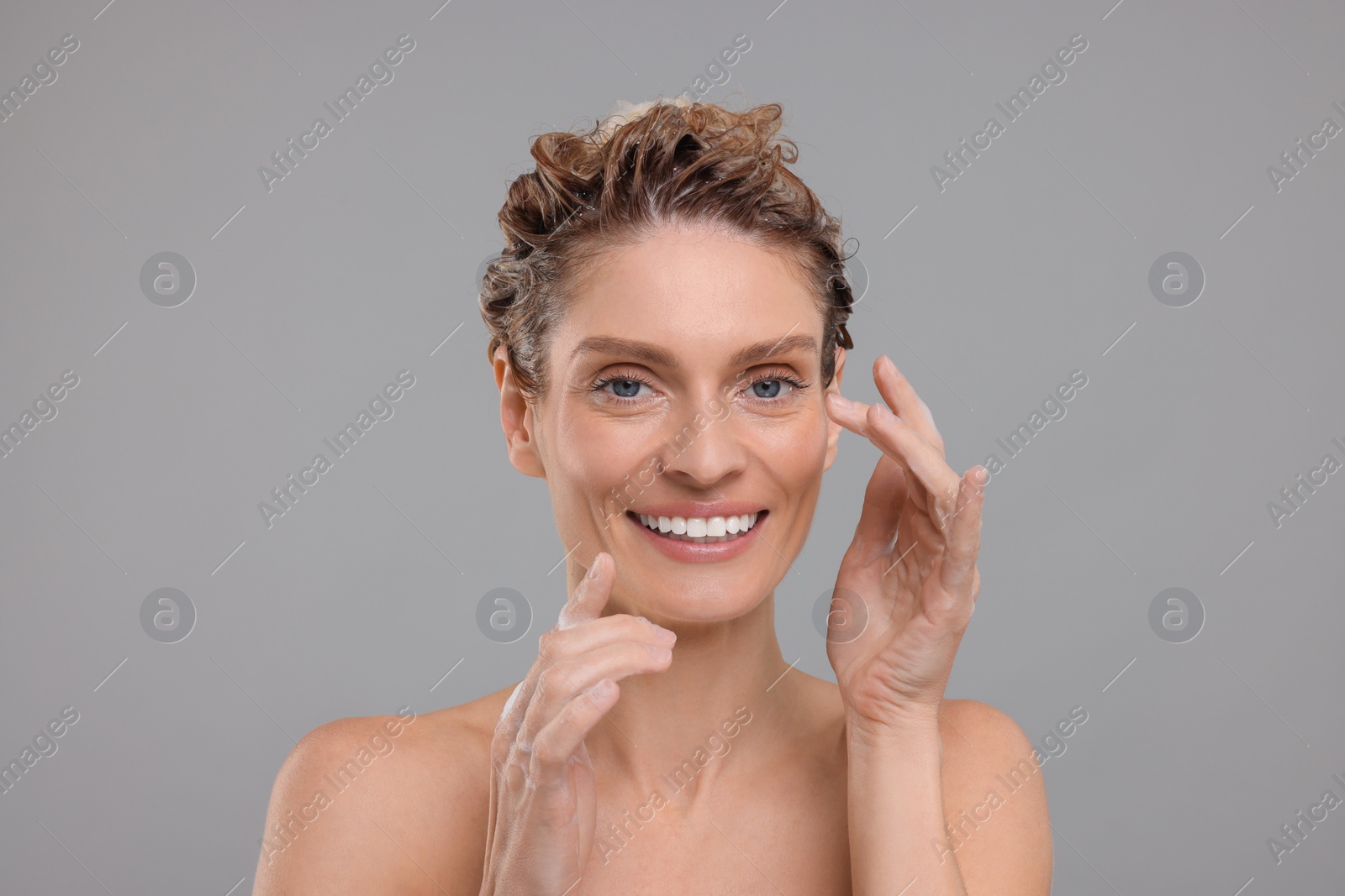 Photo of Portrait of beautiful happy woman washing hair on light grey background