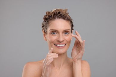 Portrait of beautiful happy woman washing hair on light grey background