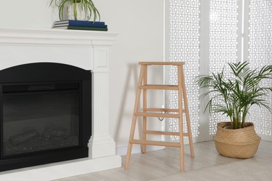 Photo of Wooden folding ladder between fireplace and potted plant in room