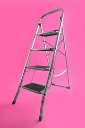 Photo of Modern metal stepladder on pink background. Construction tool