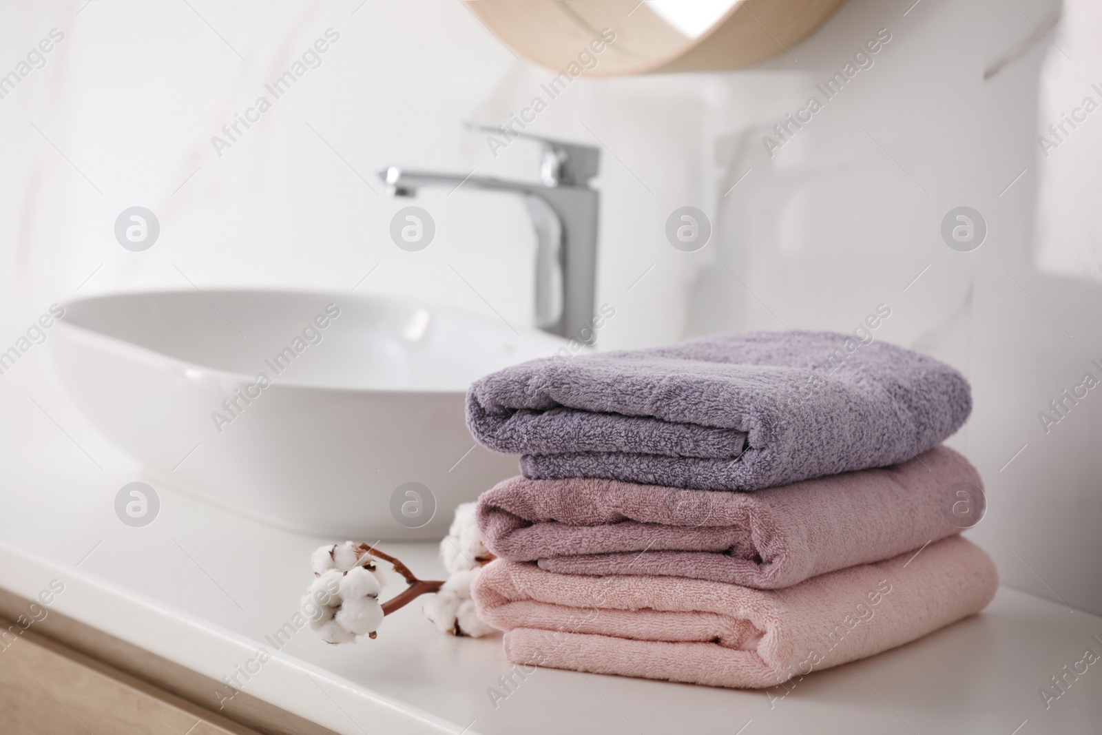 Photo of Stack of fresh towels and cotton flowers on countertop in bathroom