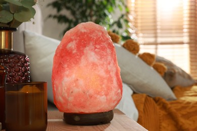 Photo of Beautiful Himalayan salt lamp on wooden nightstand in bedroom