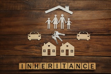 Photo of Word Inheritance made with cubes and different cutouts on wooden background, flat lay