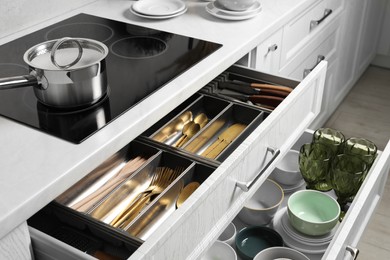 Photo of Ceramic dishware and cutlery in drawers in kitchen