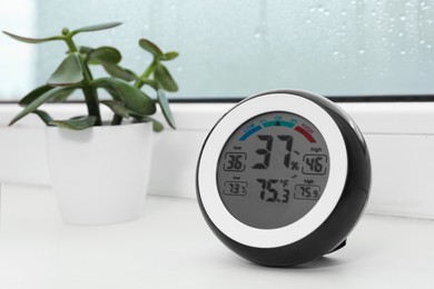 Photo of Digital hygrometer with thermometer and green plant on sill near window indoors