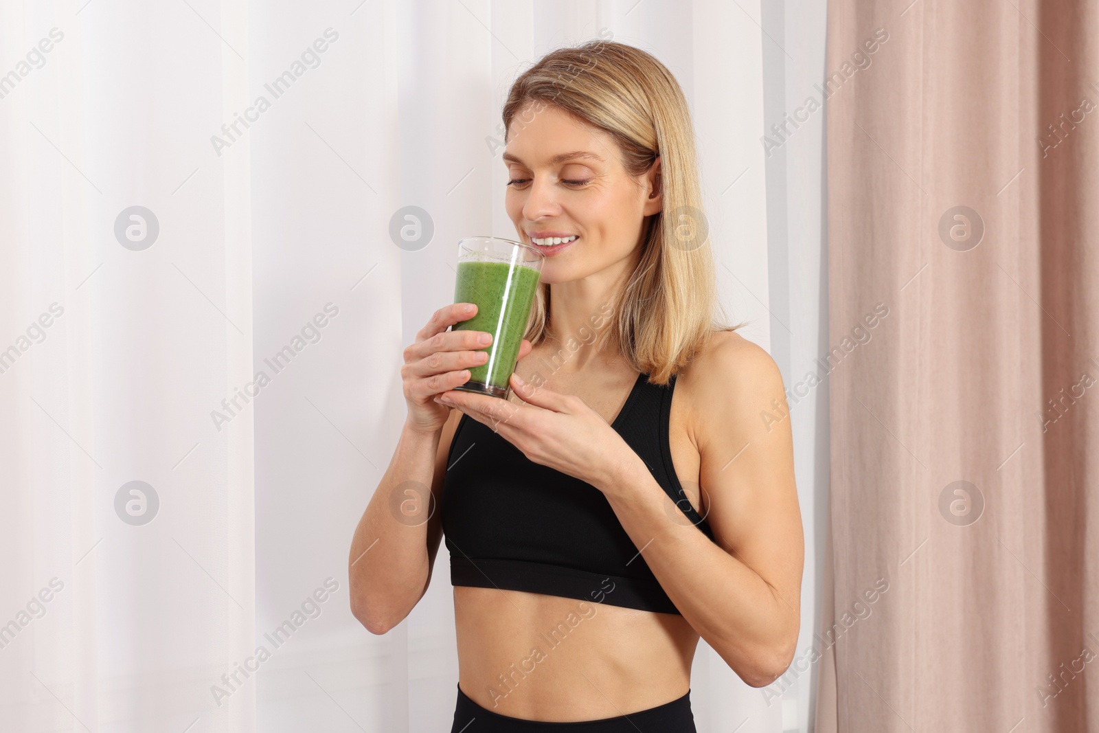 Photo of Young woman in sportswear with glass of fresh smoothie at home