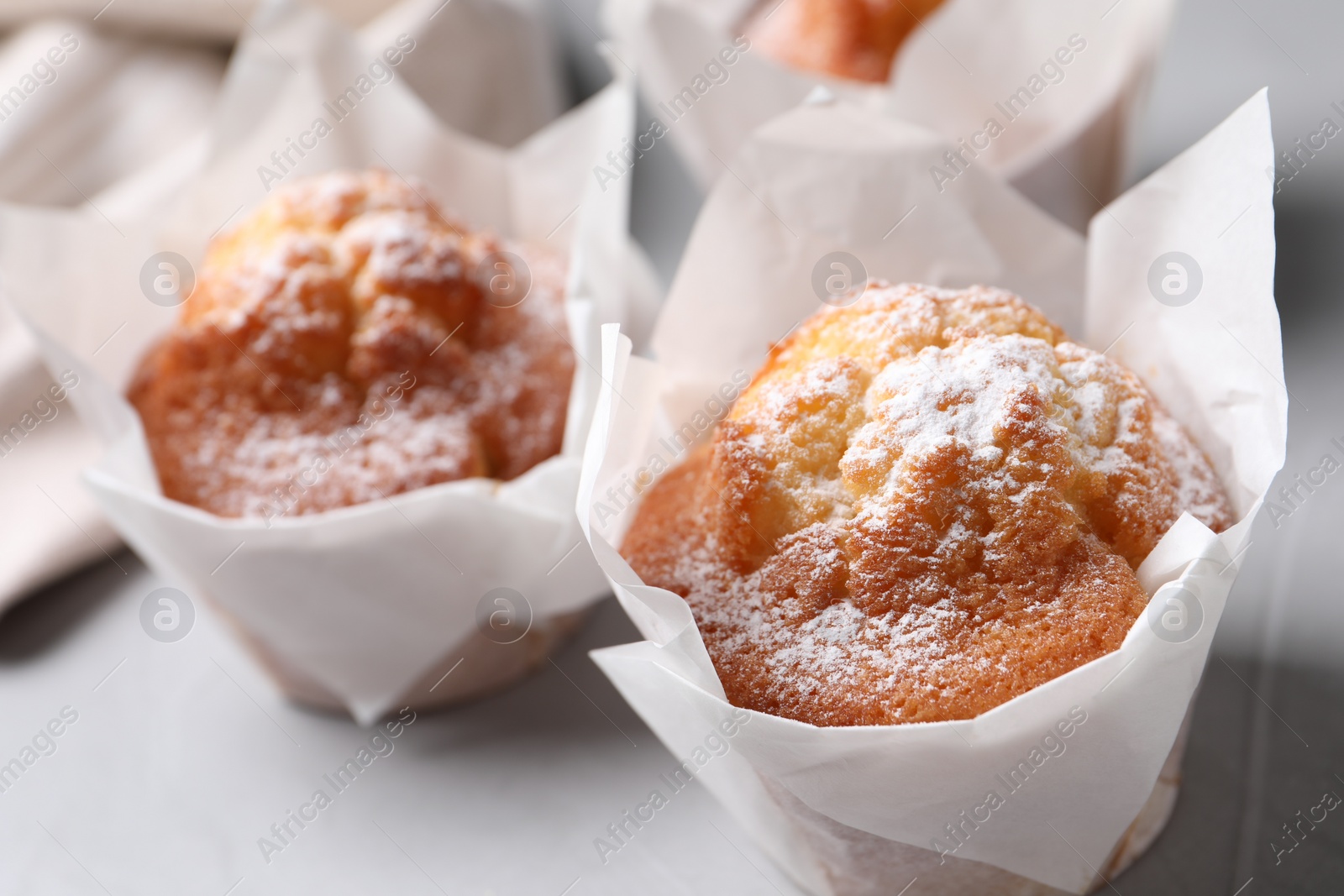 Photo of Delicious muffins with powdered sugar on light table, closeup